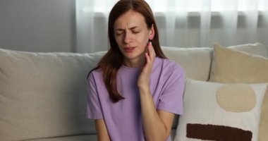 Ses geliyor. Evdeki koltukta kulağına dokunan endişeli kadın, kamera ilerliyor.