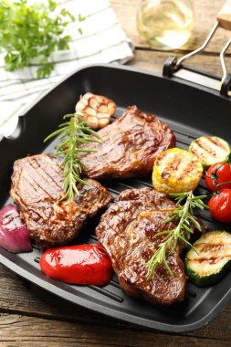 Tavada ızgara biftek, biberiye ve sebzeler ahşap masada, yakın plan.