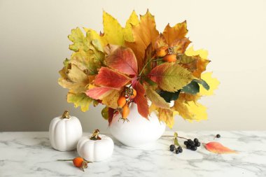 Beyaz mermer masa üzerinde kuru yapraklar, böğürtlenler ve dekor vazosu ile sonbahar kompozisyonu