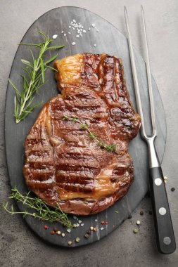 Lezzetli ızgara biftek, otlar, baharatlar ve çatal, gri desenli masa, düz yatış.