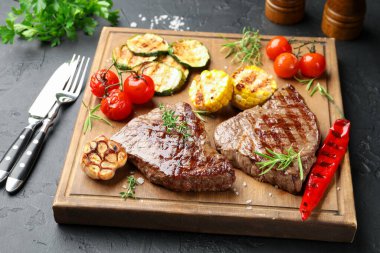 Bitki ve sebzeli leziz ızgara biftekler, koyu dokulu masa, yakın plan.