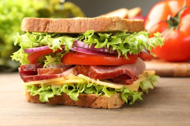 Delicious sandwich with ham, cheese and vegetables on wooden table, closeup