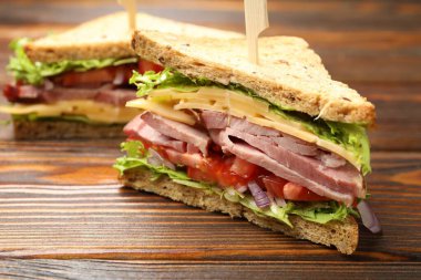 Delicious sandwiches with ham, cheese and vegetables on wooden table, closeup
