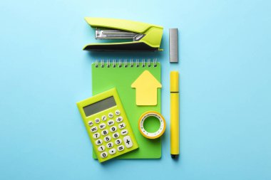 Yellow stapler and other stationery on light blue background, flat lay