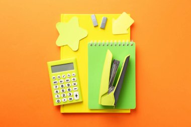 Stapler, metal staples, notebooks, calculator and sticky notes on orange background, top view