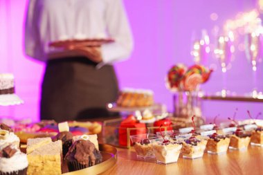 Different delicious desserts on buffet table and waiter, selective focus