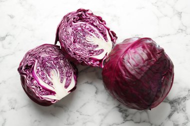 Whole and cut red cabbages on white marble table, top view