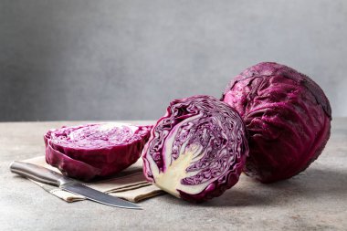 Whole and cut red cabbages with knife on grey table, closeup