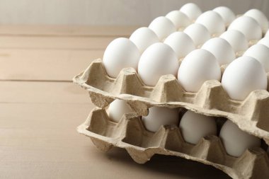 Many raw chicken eggs in cartons on wooden table, closeup