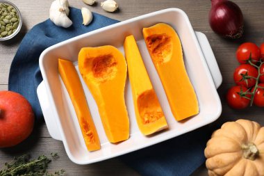 Cut pumpkin in baking dish and ingredients on wooden table, flat lay