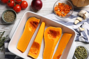 Cut pumpkin in baking dish and ingredients on wooden table, flat lay
