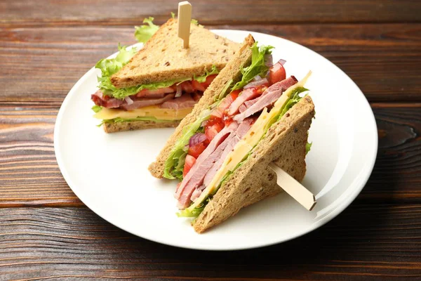 Delicious sandwiches with ham, cheese and vegetables on wooden table, closeup