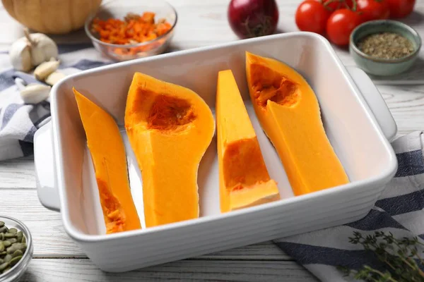 Cut pumpkin in baking dish and ingredients on wooden table, closeup