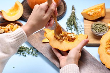 Bir kadın açık mavi arka planda kaşıkla balkabağı bağırsaklarını çıkarıyor. Yakın plan.