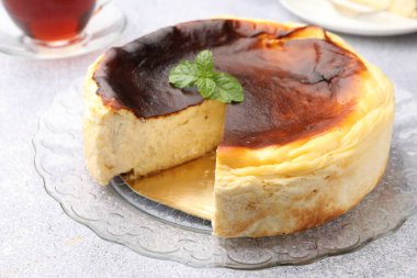 Delicious Basque cheesecake with mint and tea on light grey table, closeup
