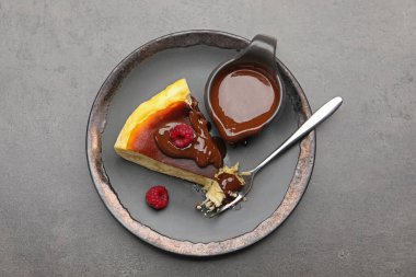 Piece of delicious Basque cheesecake with chocolate sauce and raspberries on grey table, top view