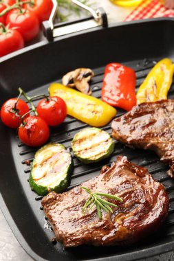 Pan with grilled beef steaks and vegetables on grey table, closeup