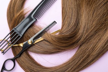 Güzel kahverengi saçlar, makas ve açık mor arkaplan tarağı, üst görünüm