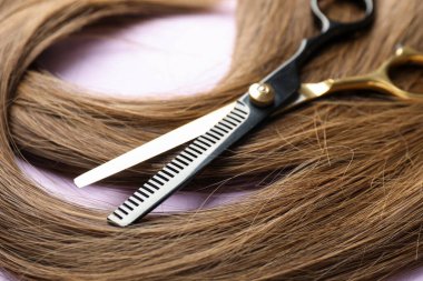 Açık mor arkaplanda güzel kahverengi saç ve makas, yakın plan.