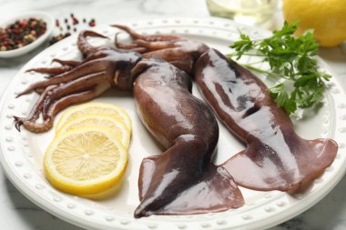 Raw squids, lemon and parsley on white marble table, closeup