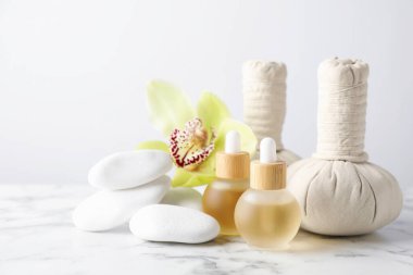Beautiful spa composition with essential oils and herbal bags on white marble table against light background, closeup