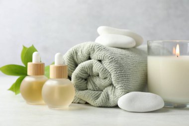 Beautiful composition with burning candle and spa stones on white table, closeup