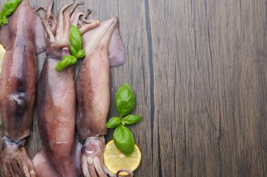 Raw squids, lemon slices and basil on wooden table, flat lay. Space for text