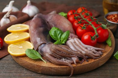 Raw squids, tomatoes, lemon slices and basil on wooden table, closeup