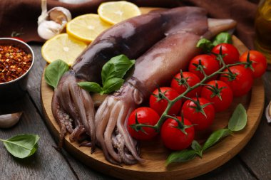 Raw squids, tomatoes, lemon slices and basil on wooden table, closeup