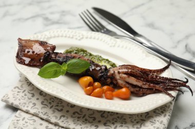 Tasty cooked squid served with sauce, tomatoes, cutlery and basil on white marble table, closeup