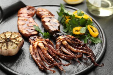 Tasty cooked squids served with garlic and salad on black table, closeup