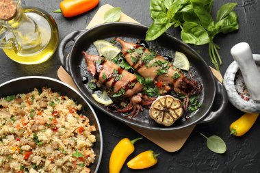 Tasty cooked squids with sauce, garlic and products on black table, flat lay
