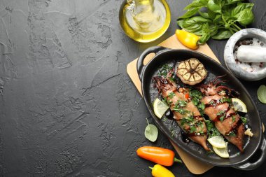 Tasty cooked squids with sauce, garlic and products on black table, flat lay. Space for text