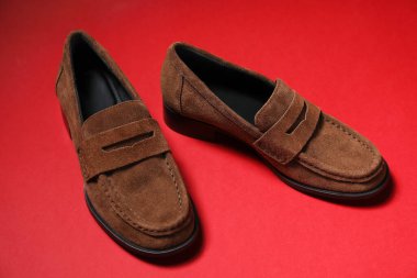 Pair of stylish brown shoes on red background, closeup
