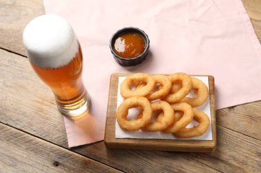 Tasty fried squid rings, sauce and glass of beer on wooden table