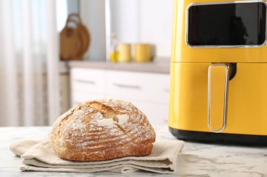 Mutfaktaki beyaz mermer masada taze pişmiş ekmek ve hava kızartma makinesi, yakın plan.