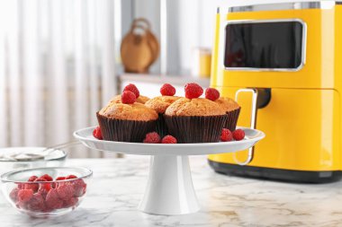 Mutfaktaki beyaz mermer masada ahududu ve hava kızartma makineli taze pişmiş muffinler.