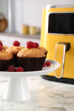 Mutfaktaki beyaz mermer masada ahududu ve hava kızartma makineli taze pişmiş muffinler.