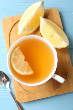 Aromatic tea in cup with lemon and spoon on light blue wooden table, top view