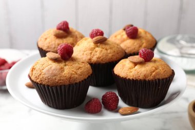 Fresh muffins with raspberries and almonds on white table, closeup