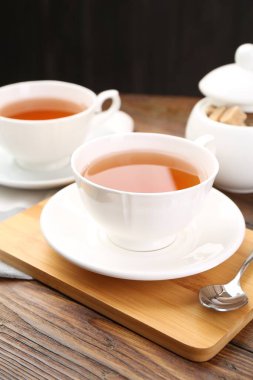 Aromatic black tea in cups and brown sugar on wooden table, closeup