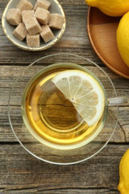 Aromatic black tea in glass cup, brown sugar and lemons on wooden table, flat lay
