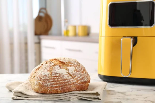 Mutfaktaki beyaz mermer masada taze pişmiş ekmek ve hava kızartma makinesi, yakın plan.