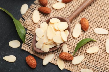 Fresh almond flakes, whole nuts and green leaves on grey table, above view
