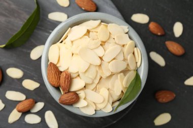 Fresh almond flakes, whole nuts and green leaves on grey table, flat lay