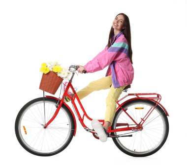 Gülen kadın beyaz arka planda bir sepet çiçekle bisiklet sürüyor.