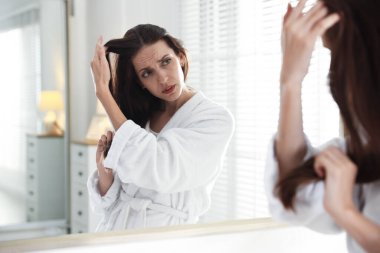 Saç dökülme sorunu olan kadın aynaya bakıyor.