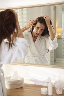 Saç dökülme sorunu olan kadın aynaya bakıyor.