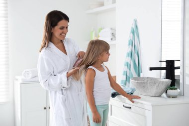 Anne banyoda kızının saçını tarıyor.