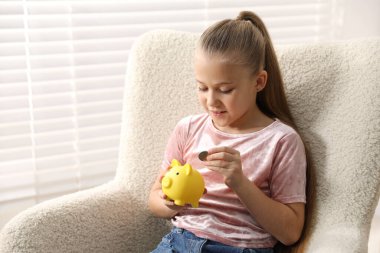 Küçük kız cep harçlığını evdeki kumbaraya yatırıyor.